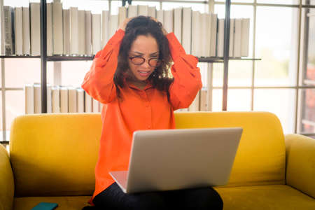 Beautiful Latin woman working with laptop on sofa with stressed feeling