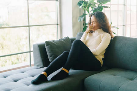 Latin woman sitting on sofa at home with illness feelingの写真素材