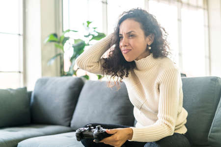 Laitin woman playing videogames with hands holding joystick on sofa at home
