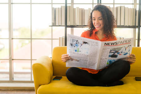 Latin America woman reading newspaper on sofa at homeの写真素材