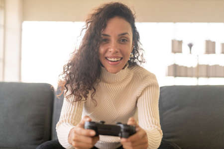 Laitin woman playing videogames with hands holding joystick on sofa at home