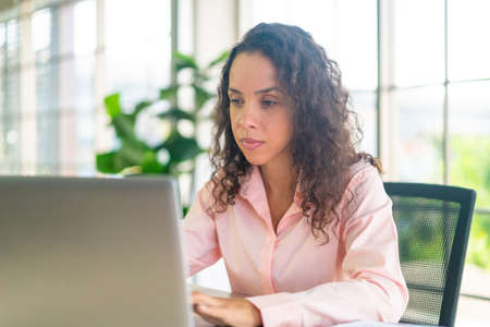 Latin woman working with laptop and paper on working space at home