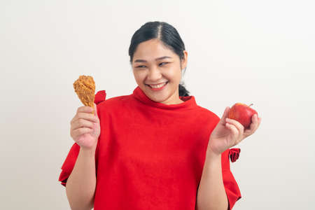 portrait Asian woman with fried chicken and apple on hand for choiceの写真素材