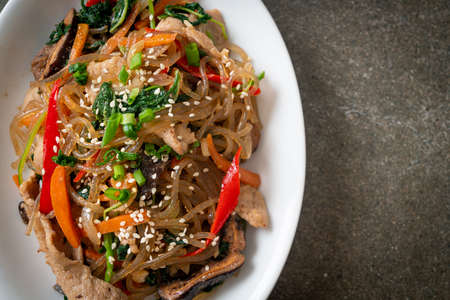 japchae or stir-fried Korean vermicelli noodles with vegetables and pork topped with white sesame -...