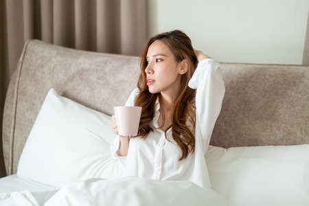 portrait beautiful Asian woman wake up and holding coffee cup or mug on bed in the morningの写真素材
