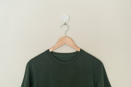 dark green t-shirt hanging with wood hanger on wall