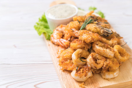 fried seafood (squids, shrimps, mussels) with sauce on wooden boardの写真素材