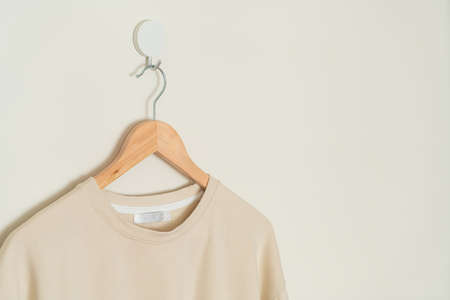 beige t-shirt hanging with wood hanger on wallの写真素材