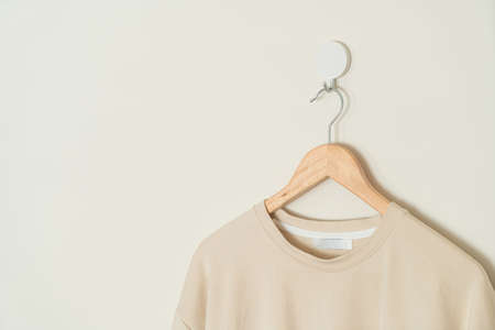 beige t-shirt hanging with wood hanger on wall