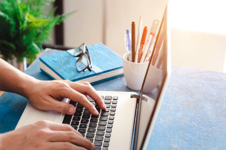 Close up shot of  male hands typing on laptop while sitting at office desk indoors, man fingers tapping and texting on computer keyboard while working in cabinet, Work concept.の写真素材