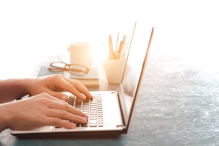 Close up shot of male hands typing on laptop while sitting at office desk indoors, man fingers tapping and texting on computer keyboard while working in cabinet, Work concept.の写真素材
