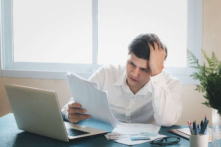Young Asian men are stressed out in business office. Looking at expense bill and the other hand on head, thinking about finding money to pay credit card debt and all bills. Concept financial problems.の写真素材