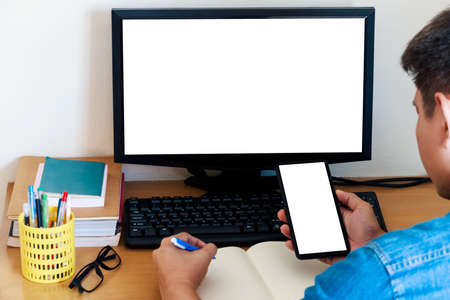 Mockup Copy Space Computer screen and smartphone screen Concept , a man's hand using a smartphone on internet websites at the office, keyboards on computer with blank copy screen for your advertising content.の写真素材