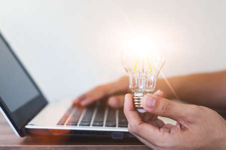 Hand holding a light bulb and working on a laptop computer, Concept of inspirational ideas creativity and technological innovation of the future.の写真素材