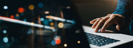 young man hand working on a laptop, bokeh blurred at night For text copy space, image size horizontalの写真素材
