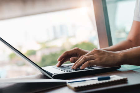 young man using laptop computer and mobile phone When looking for financial information in business, work at the desk. Writing with a pen, studying remotely from home and working from home.の写真素材