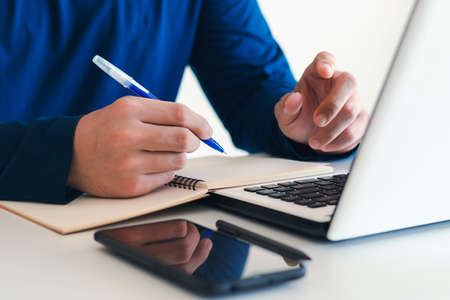 Businessman taking notes Summarize the meeting online with laptop, working alone, sitting at your...