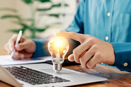 Successful Innovation through ideas and inspiration ideas. Human hand holding light bulb to illuminate, idea of creativity and inspiration concept of sustainable business development.の写真素材