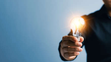 Successful Innovation through ideas and inspiration ideas. Human hand holding light bulb to illuminate, idea of creativity and inspiration concept of sustainable business development.の写真素材