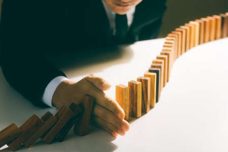 Risk management, business man hand Stop the continuous falling of wooden dominoes, stop the impact of the business crisis. hedging Solving business problems for success.の写真素材