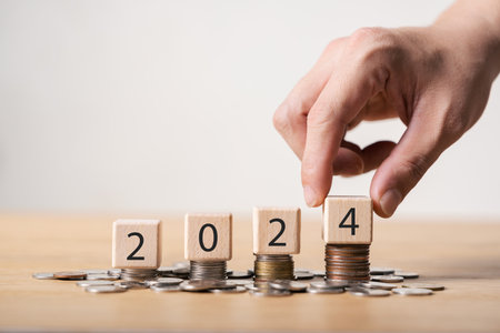 2024 new year goals planning concept, wooden cubes on stack of coins, positive indicator 2024, investment finance planning for the new year 2024.の写真素材