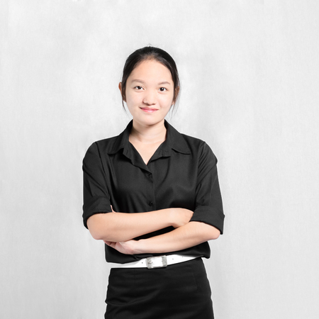 Portrait of a beautiful asian girl cross one 'arms in black uniform. Isolated on grey backgroundの写真素材