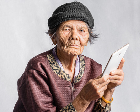 Portrait of a senior woman confused with tablet in vintage costume. Isolated on grey backgroundの写真素材