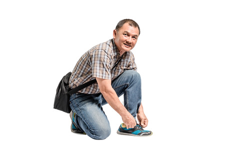 Portrait of a happy mature man in scott shirt and blue jeans tying his shoes. Isolated full length on white background with copy space and clipping pathの写真素材