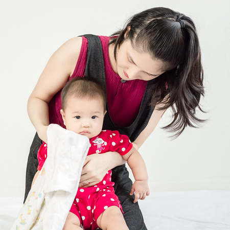 Mother wipes snivels a little adorable infant baby girl with hankerchief and looking in camera indoorsの写真素材