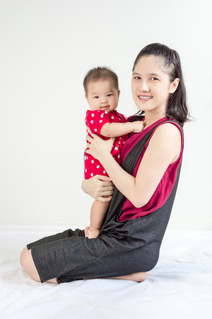 Portrait of happy asian mother hugging her cute little baby and looking in camera indoorsの写真素材