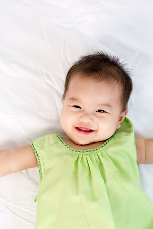 Portrait of a little adorable infant baby girl lying on back on bed and looking in camera indoorsの写真素材