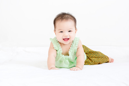 Portrait of a little adorable infant baby girl with saliva lying on the tummy on bed and looking in camera indoorsの写真素材