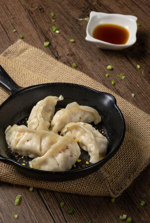 Gyozas, fried japanese dumplings on cast-iron pan served with soy sauce. wooden texture background.の写真素材