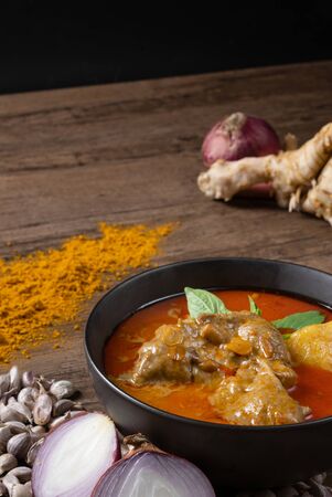 Chicken massaman curry in black bowl with herb and spices on wooden background. Thai authentic food call massaman kai.の写真素材