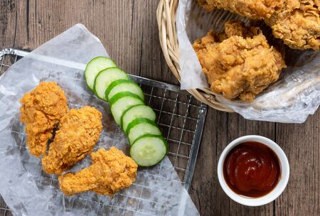 Crispy fried chicken on Sieve and wicker basket serve with cucumber and ketchup on wooden background. top view. flat lay.の写真素材