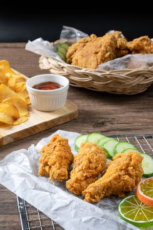 Crispy fried chicken on Sieve and wicker basket serve with cucumber and potato chips on Wood cutting board serve with ketchup on wooden background.の写真素材