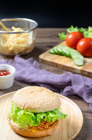 Crispy fried chicken burger on Round Wood plate served with french fries and ketchup on wooden background.の写真素材
