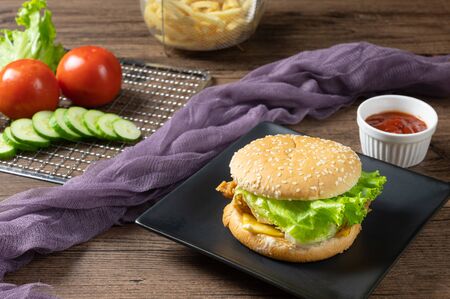 Crispy fried chicken burger on black plate served with french fries and ketchup on wooden background.の写真素材