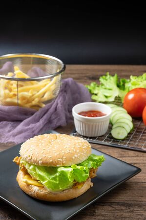 Crispy fried chicken burger on black plate served with french fries and ketchup on wooden background.の写真素材