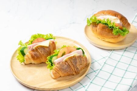 Delicious croissants sandwichs with fresh Ham, cheese, tomato, cucumber, lettuce and Sub sandwich with fresh salad, Ham , cheese served on round wooden plate. white background.の写真素材