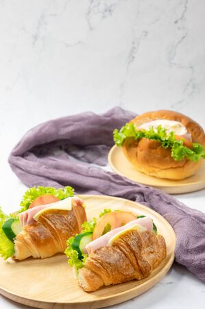Delicious croissants sandwichs with fresh Ham, cheese, tomato, cucumber, lettuce and Sub sandwich with fresh salad, Ham , cheese served on round wooden plate. white background.の写真素材