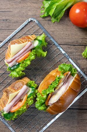 Delicious croissants sandwichs with fresh Ham, cheese, tomato, cucumber, lettuce and Sub sandwich with fresh salad, Ham , cheese served on sieve. wooden background Top view. Flat lay.の写真素材
