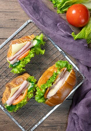 Delicious croissants sandwichs with fresh Ham, cheese, tomato, cucumber, lettuce and Sub sandwich with fresh salad, Ham , cheese served on sieve. wooden background Top view. Flat lay.の写真素材