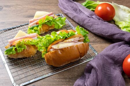 Delicious croissants sandwichs with fresh Ham, cheese, tomato, cucumber, lettuce and Sub sandwich with fresh salad, Ham , cheese served on sieve. wooden background.の写真素材