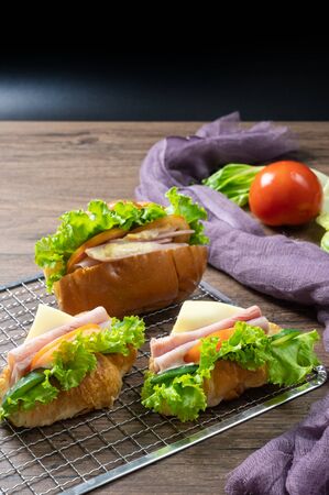 Delicious croissants sandwichs with fresh Ham, cheese, tomato, cucumber, lettuce and Sub sandwich with fresh salad, Ham , cheese served on sieve. wooden background.の写真素材
