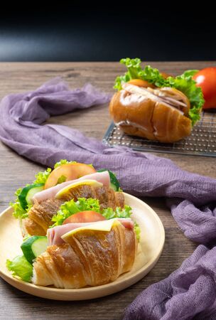 Delicious croissants sandwichs with fresh Ham, cheese, tomato, cucumber, lettuce served on round wooden plate and Sub sandwich with fresh salad, Ham , cheese served on sieve. wooden backgroundの写真素材