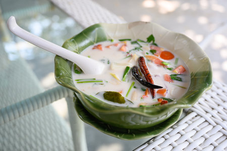 A bowl of Tom Kha, a traditional Thai coconut soup with mixed seafood, served in a green ceramic bowl on a woven mat.の写真素材