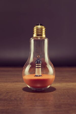 Lighthouse on orange sand in spiral bulb on wooden tableの写真素材