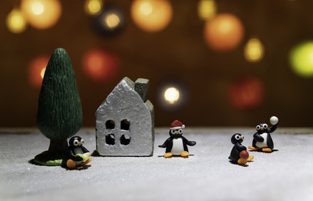 Penguins in different acting around the house and tree on ice floor