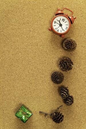 Red alarm clock with pine cone and green gift box on cork backgroundの写真素材